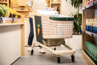 a person pushes a smart shopping cart with a carrot logo on the side