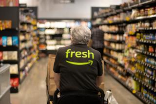 An Amazon Fresh worker pushes a cart down a store aisle.