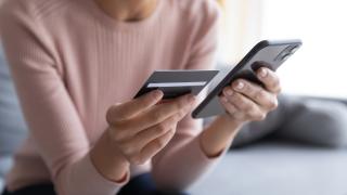 A person holds a cell phone and a credit card.
