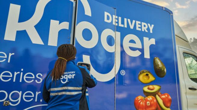 A Kroger employee stands in front of a blue truck that say "Delivery Kroger." 