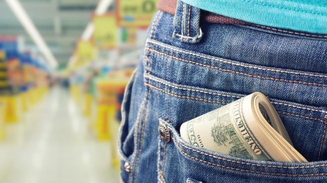 A person in a grocery store has cash in their pocket.